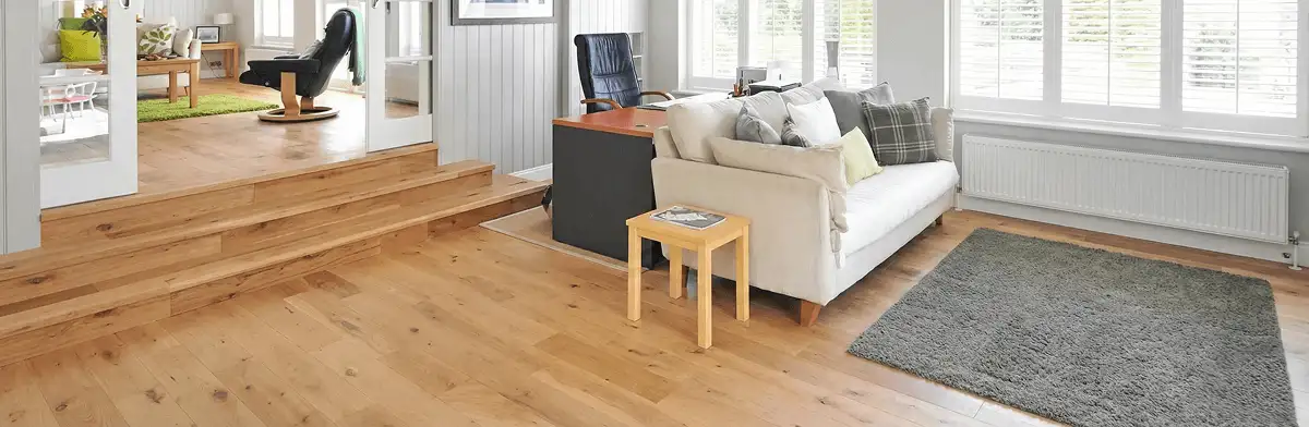 A modern living room with professionally installed laminate flooring, a beige sofa, a small side table, a gray rug, and large windows with white shutters in Dover, DE